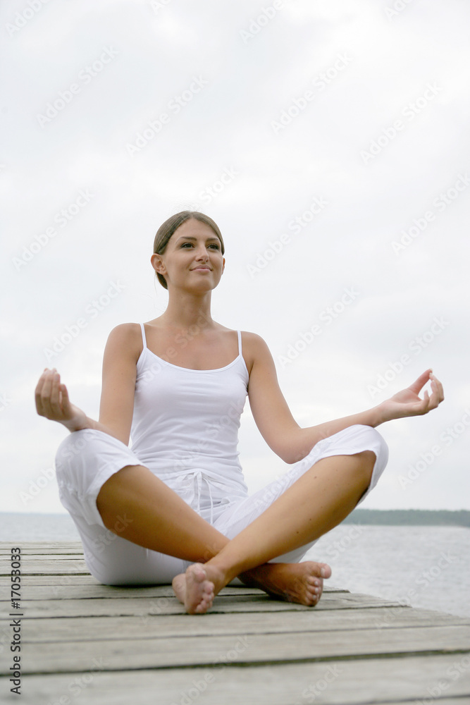 Portrait d'une femme méditant assise sur un ponton