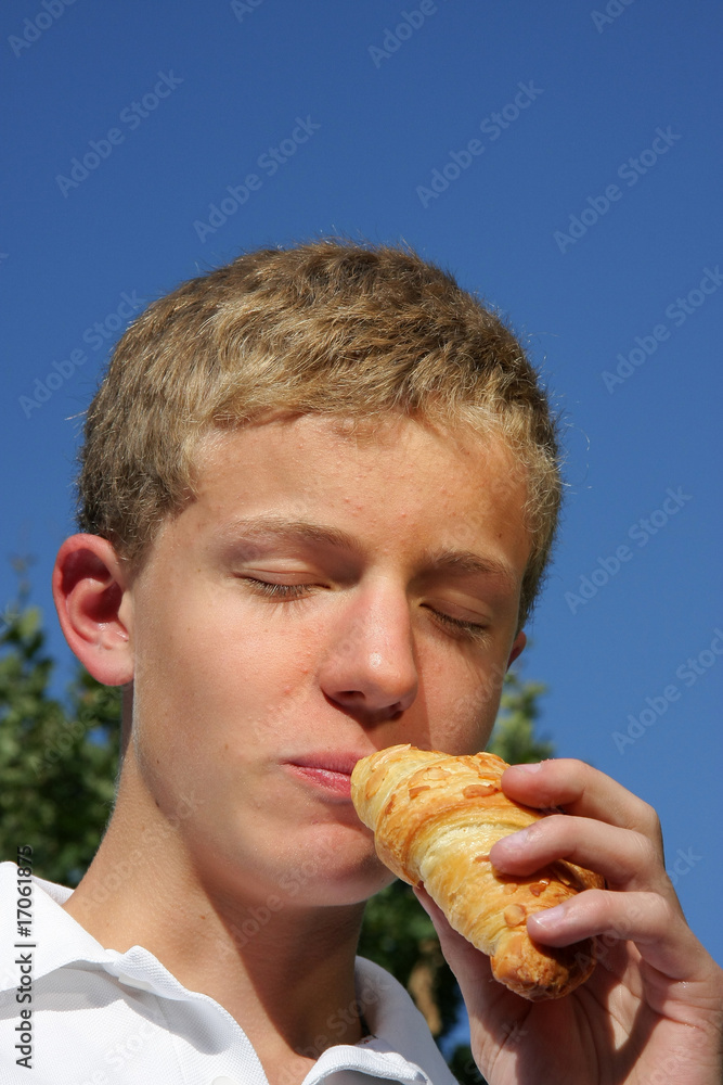 Jugendlicher geniesst Croissant mit geschlossenen Augen Jugendlicher geniesst Croissant mit geschlossenen Augen