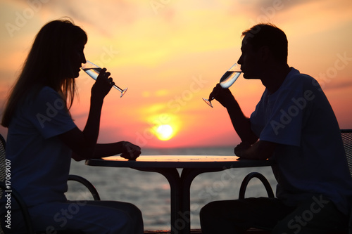 Female and man's silhouettes on sunset behind table drink from g