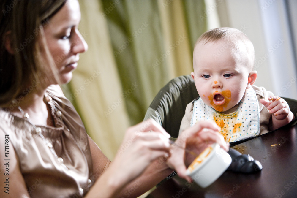 Mother feeding hungry six month old baby solid food Mother feeding hungry six month old baby solid food