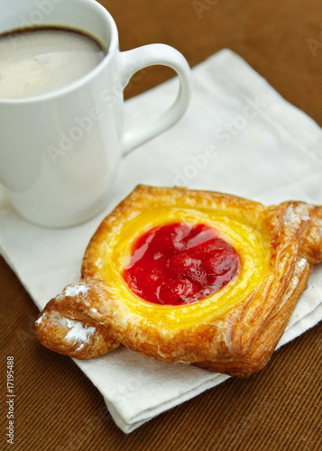 A cherry danish with a cup of hot  frothy coffee