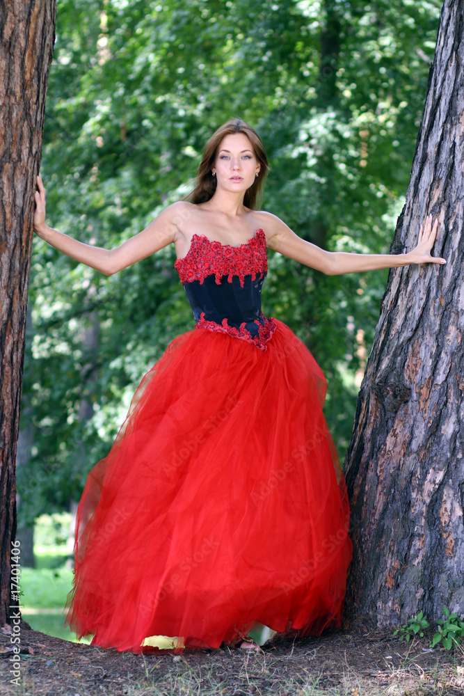 woman in a red dress standing among trees in park
