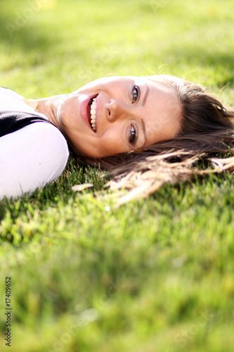 Cute young female lying on grass field at the park .