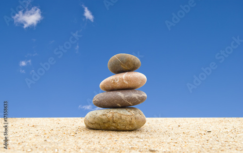 The balanced stones on sand against the blue sky