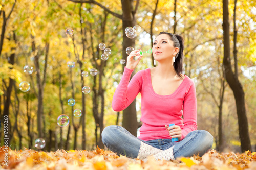 Fototapeta Naklejka Na Ścianę i Meble -  Young woman blowing soap bubble in the autumn park