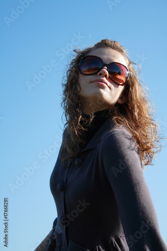 girl in sun glasses poses against the blue sky