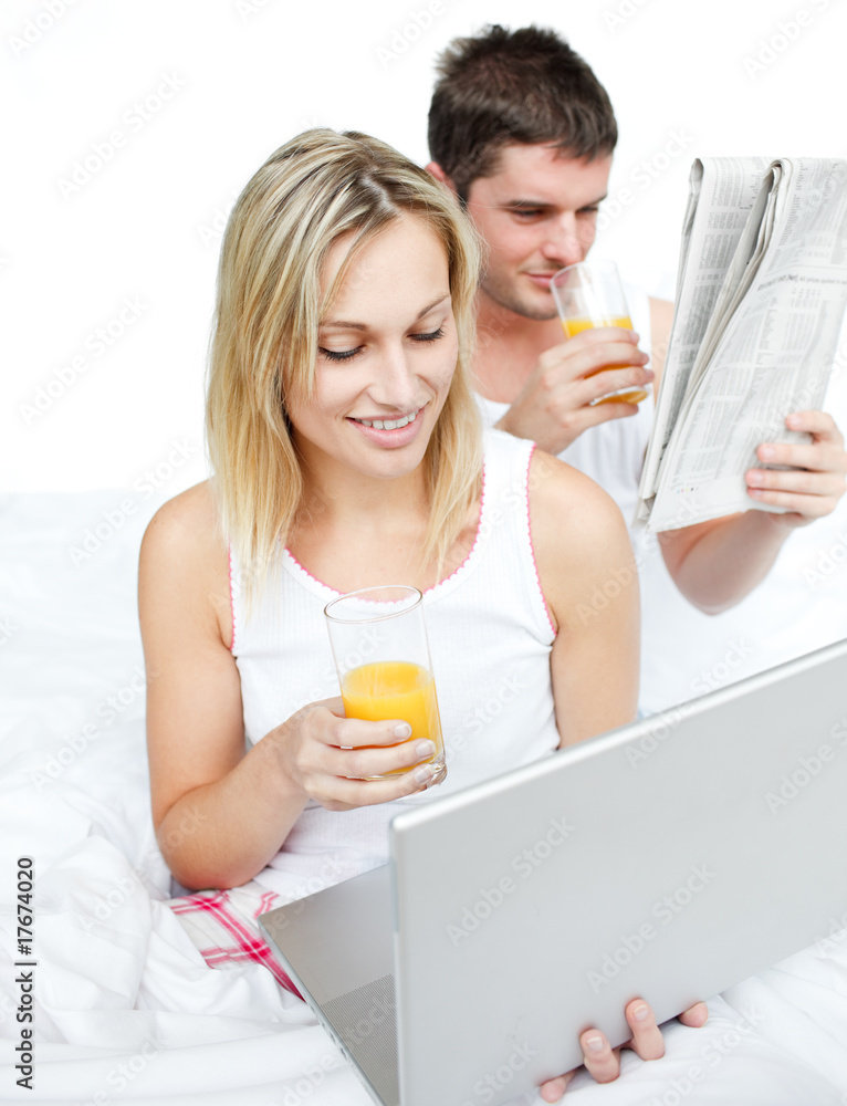 Couple reading a newspaper and using a laptop in bed Couple reading a newspaper and using a laptop in bed