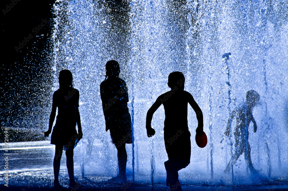 Silhouettes of Children playing in a fountain on a hot day