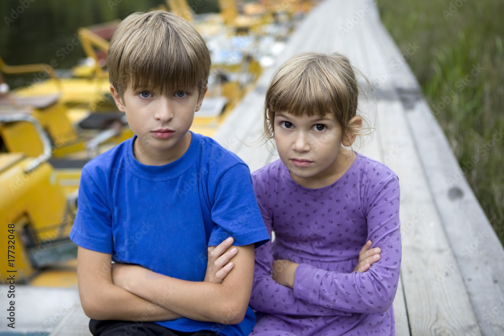 Fototapeta premium serious brother and sister sitting on piers