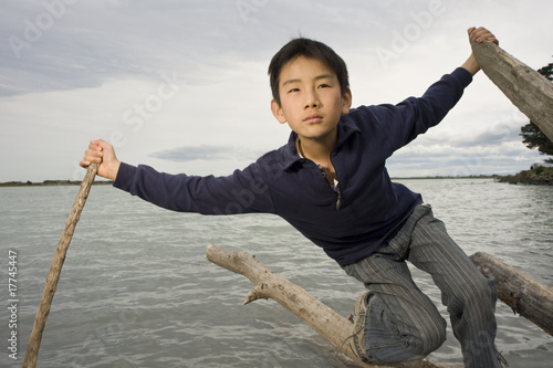 young Asian boy balancing on log in water