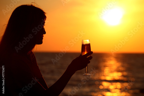 Female silhouette on sea sunset with glass in hand