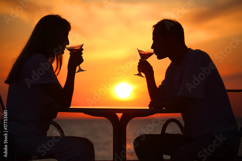 Female and man's silhouettes on sunset  drink from glasses