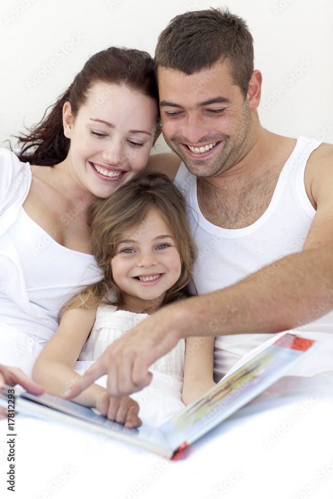 Portrait of a girl reading with her parents in bed Portrait of a girl reading with her parents in bed