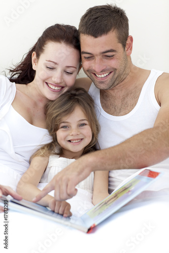 Portrait of a girl reading with her parents in bed