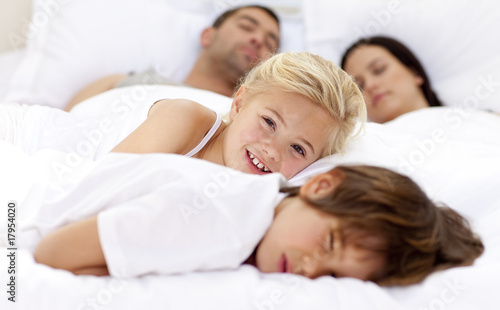 Smiling daughter relaxing with her brother and parents in bed