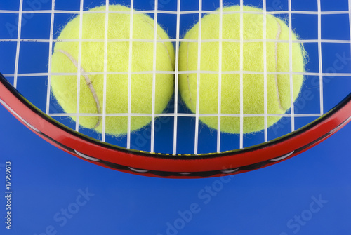 Tennis balls is under a tennis racket on a blue background. © Margaryta Vakhterova