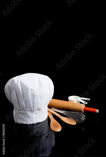 A chef's toque with kitchen utensils on black