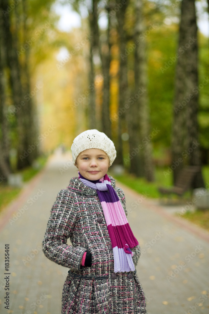 smiling cute girl in coat looking forward standing in park