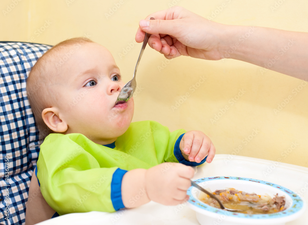 Mother feeding little baby girl in a highchair Mother feeding little baby girl in a highchair