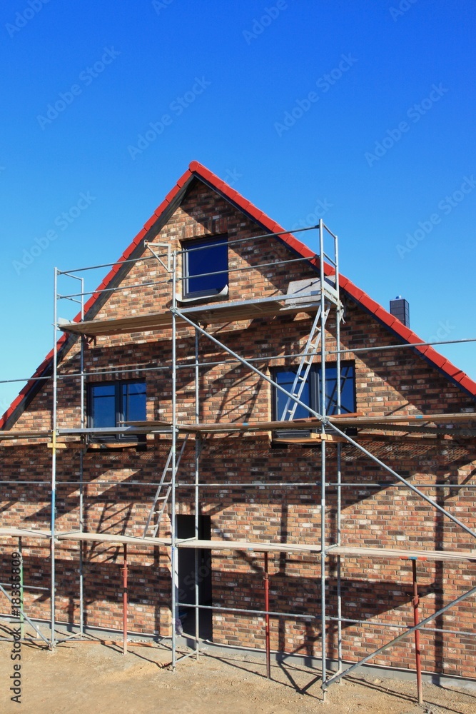 Neubau Baugerüst Einfamilienhaus vor blauem Himmel Neubau Baugerüst Einfamilienhaus vor blauem Himmel