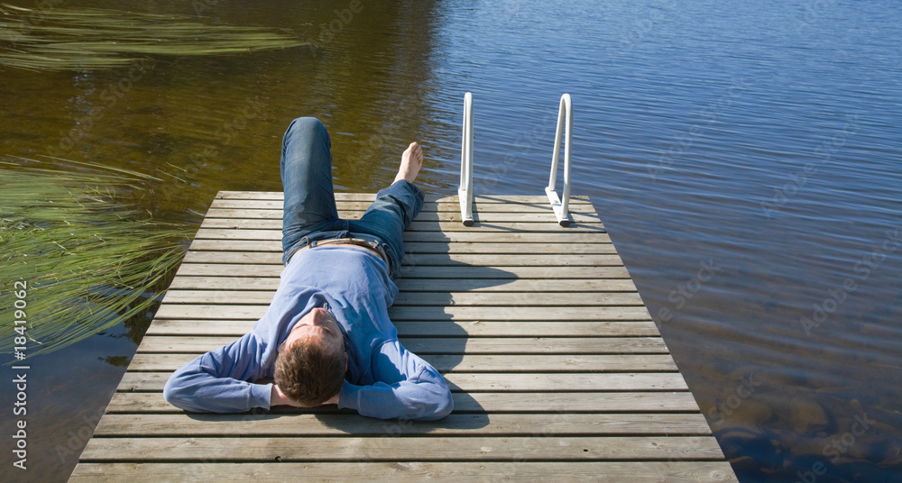 Northern summer - middle age man laying on an old wooden pier, s Northern summer - middle age man laying on an old wooden pier, s