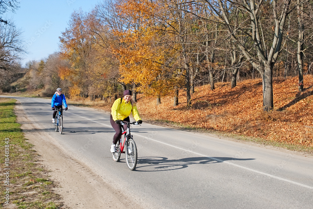 Obraz premium adults riding bicycles on road with autumn trees on sunny day