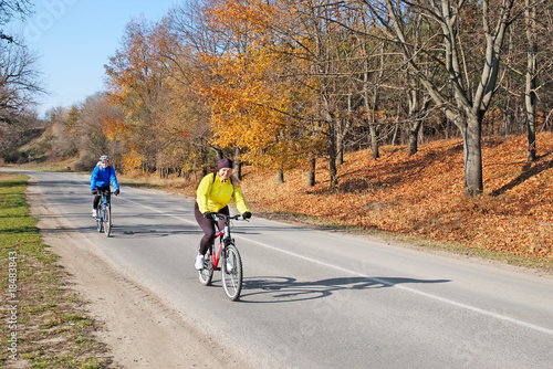 adults riding bicycles on road with autumn trees on sunny day