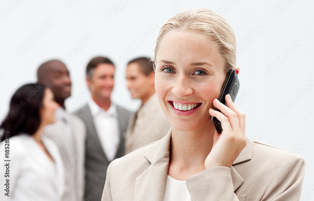 Blonde businesswoman on mobile with her team in the background Blonde businesswoman on mobile with her team in the background