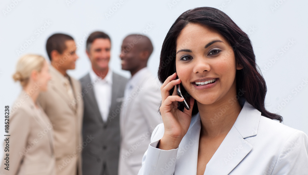 Ethnic businesswoman on phone with her team in the background Ethnic businesswoman on phone with her team in the background
