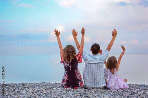 Happy family with little girl sitting on stony beach lifted hand