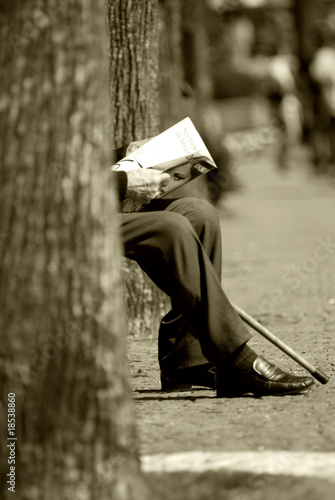 anziano signore leggendo il giornale seduto su una panchina photo