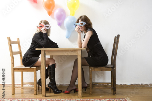 Young women with paper glasses sitting at table
