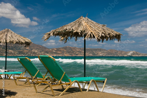 Green beachchairs together with palm umbrella photo