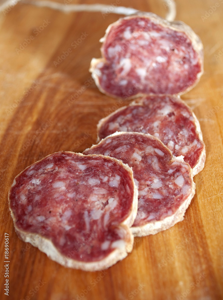 Closeup of italian typical salami and slices on wood trencher Closeup of italian typical salami and slices on wood trencher