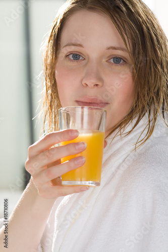 Frau im Bademantel trinkt ein Glas Orangensaft