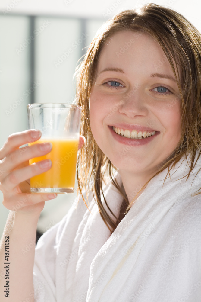 Frau im Bademantel trinkt ein Glas Orangensaft Frau im Bademantel trinkt ein Glas Orangensaft