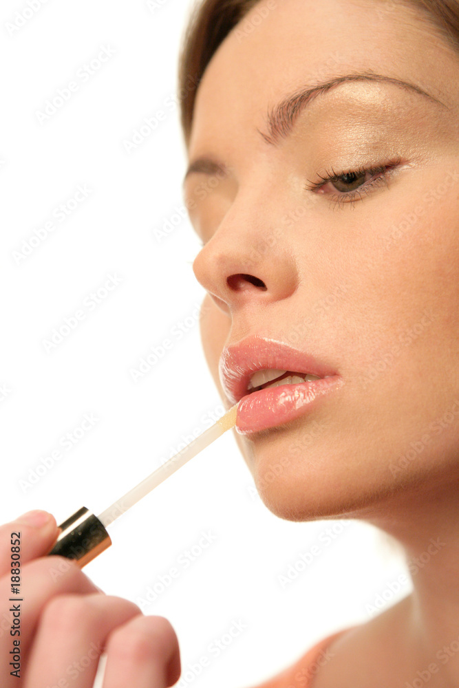 Close-up portrait of young woman applying lip gloss