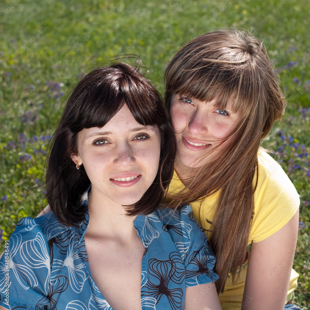 Obraz premium Two attractive sisters are sitting on the grass