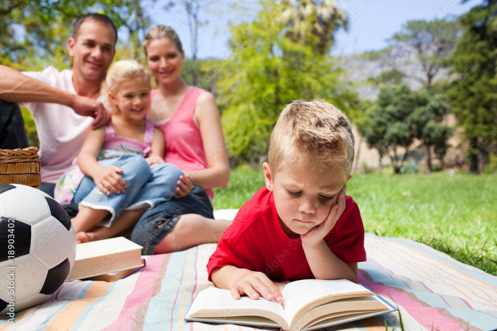 Fototapeta premium Concentrated blond boy reading while having a picnic with his fa