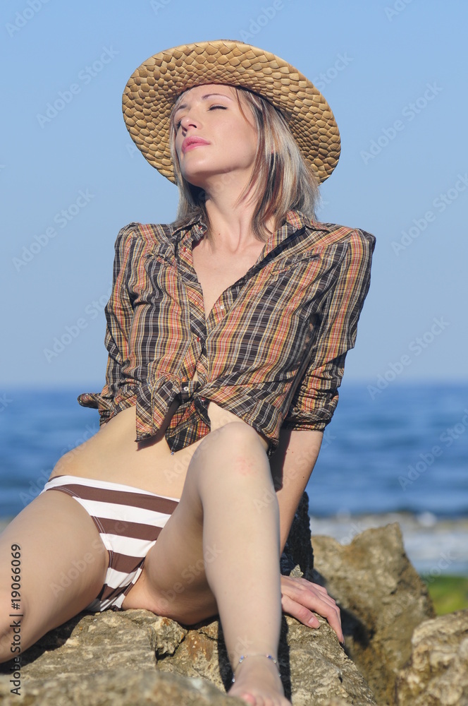 Young lady in swimsuit and hat sits on the beach