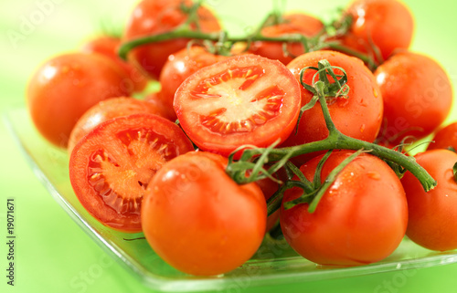 dojrzale czerwone pomidory na talerzu, na zielonym tle, grono