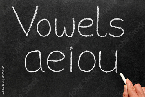 A teacher writing the five vowels letters on a blackboard.