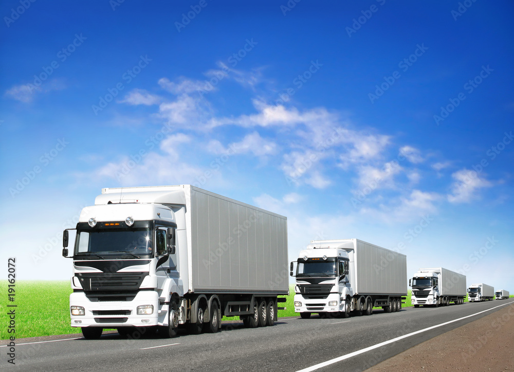 Naklejka premium caravan of white trucks on highway under blue sky