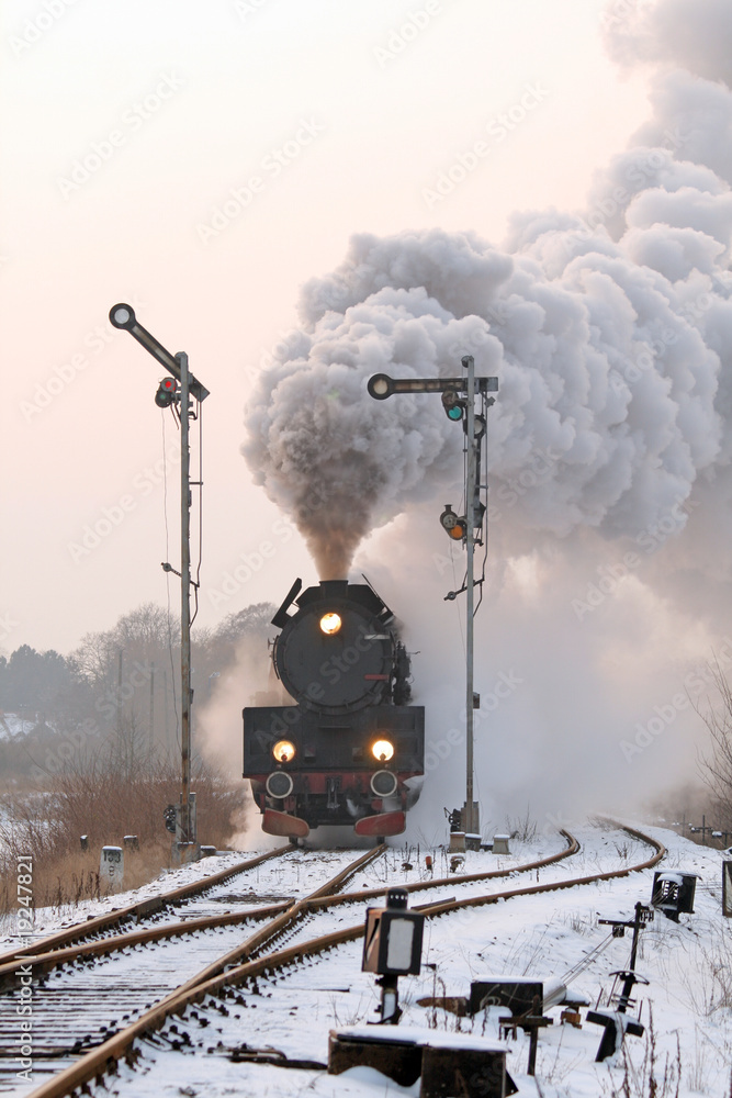 Obraz premium Retro pociąg parowy przechodzący przez wieś w okresie zimowym