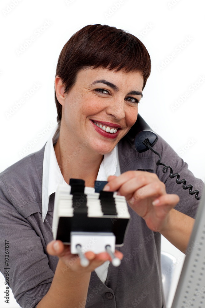 Smiling Businesswoman on phone consulting a business card holder Smiling Businesswoman on phone consulting a business card holder