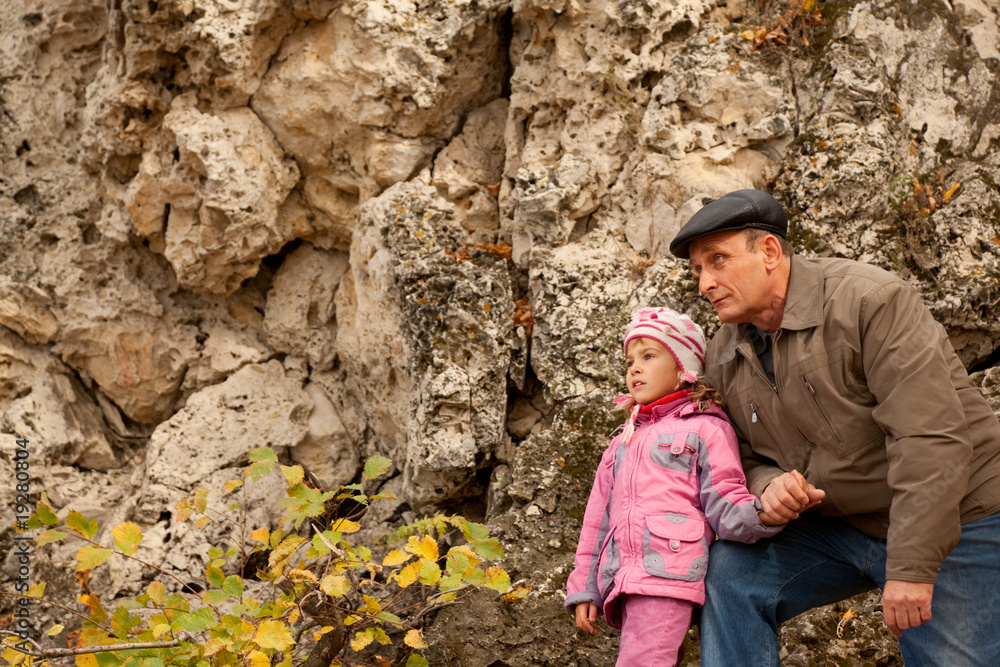 Grandfather and granddaughter near stone wall