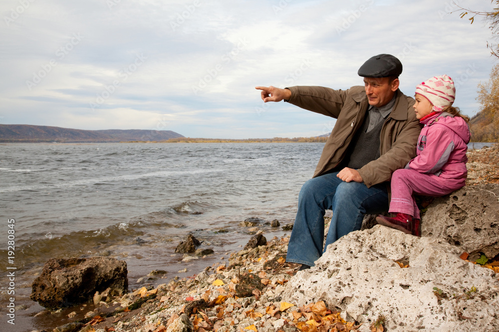 Grandfather and granddaughter sit on stone and look at lake Grandfather and granddaughter sit on stone and look at lake