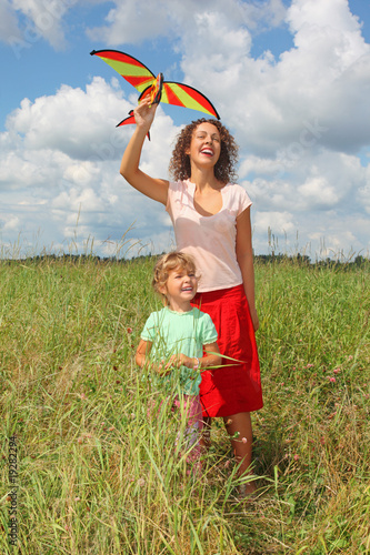 young woman and little girl plays kite on meadow