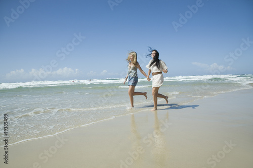 Fotografia two sisters running on beach holding hands