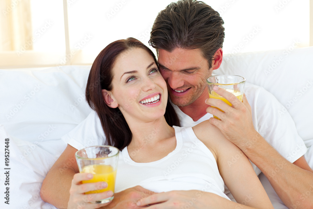 Young couple drinking orange juice lying on their bed Young couple drinking orange juice lying on their bed